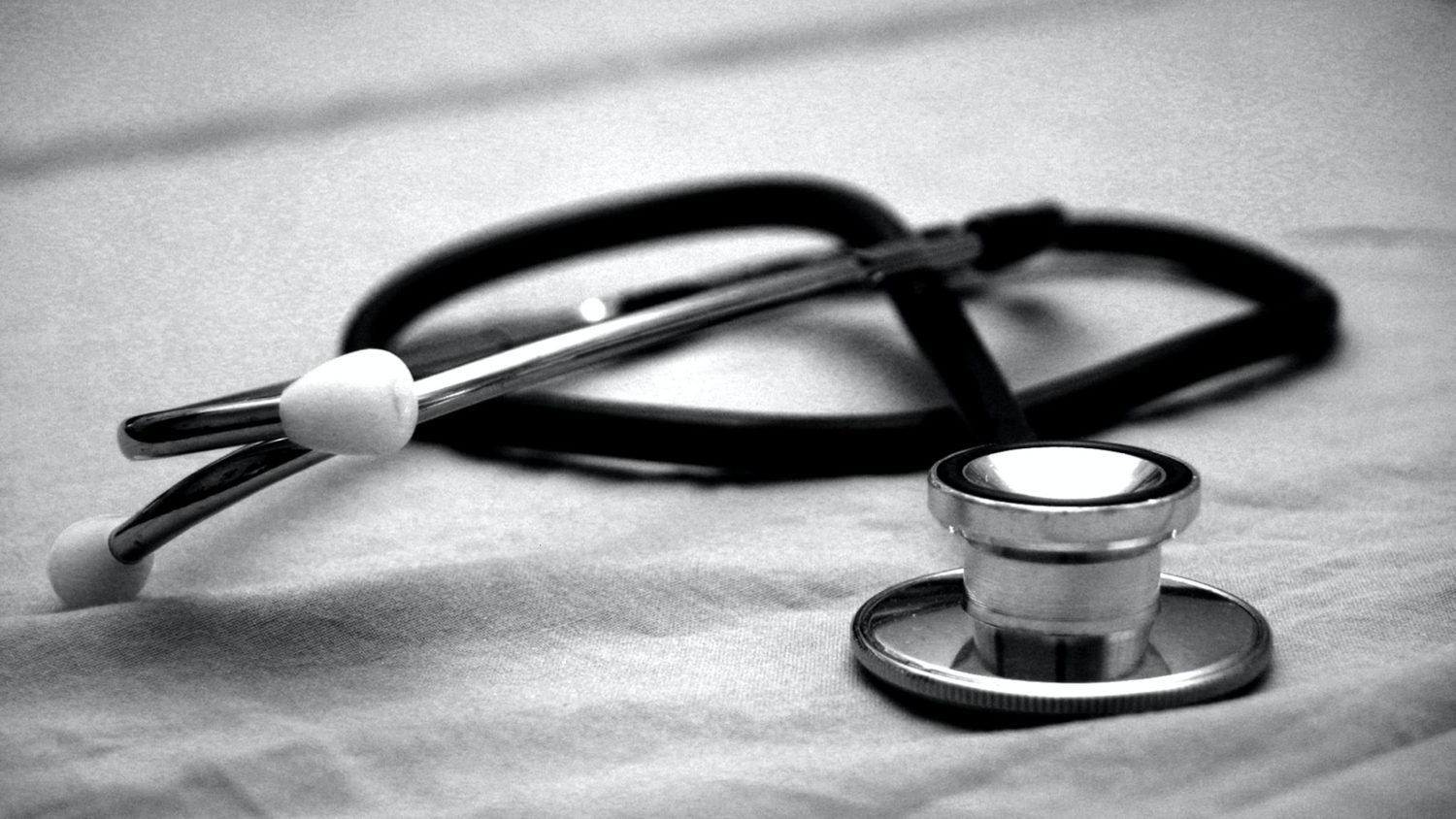 A black and white image of a stethoscope resting on a cloth-covered surface. The diaphragm is in focus, highlighting the medical instrument's importance in health care.