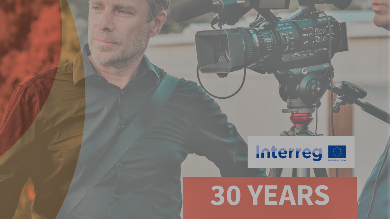 A man with a camera stands outdoors, looking thoughtful. Beside him is a cameraman adjusting a professional camera on a tripod. The text reads "Interreg 30 Years Together" with a European Union logo. The backdrop is a blurred urban setting.