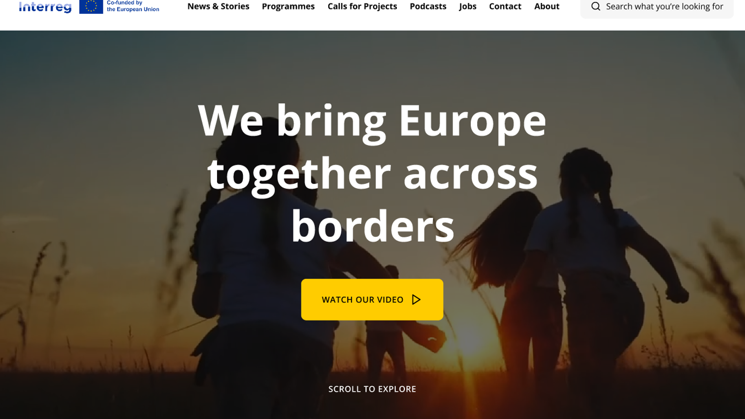 Children running in a field at sunset with the text "We bring Europe together across borders" overlaid. A yellow button below reads "Watch Our Video." The Interreg logo is at the top left.